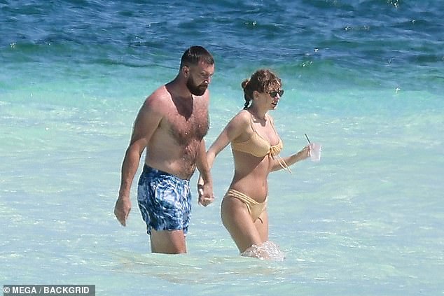 Travis took her glass with her as she waded in the Atlantic during a trip to the Bahamas with boyfriend Travis Kelce